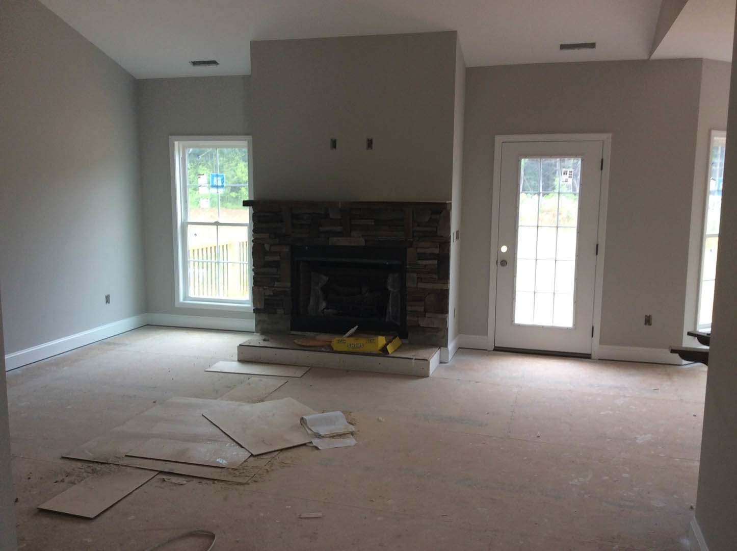 Living room with white-framed window, white door with glass panel, plaster walls, wood flooring, and stone fireplace