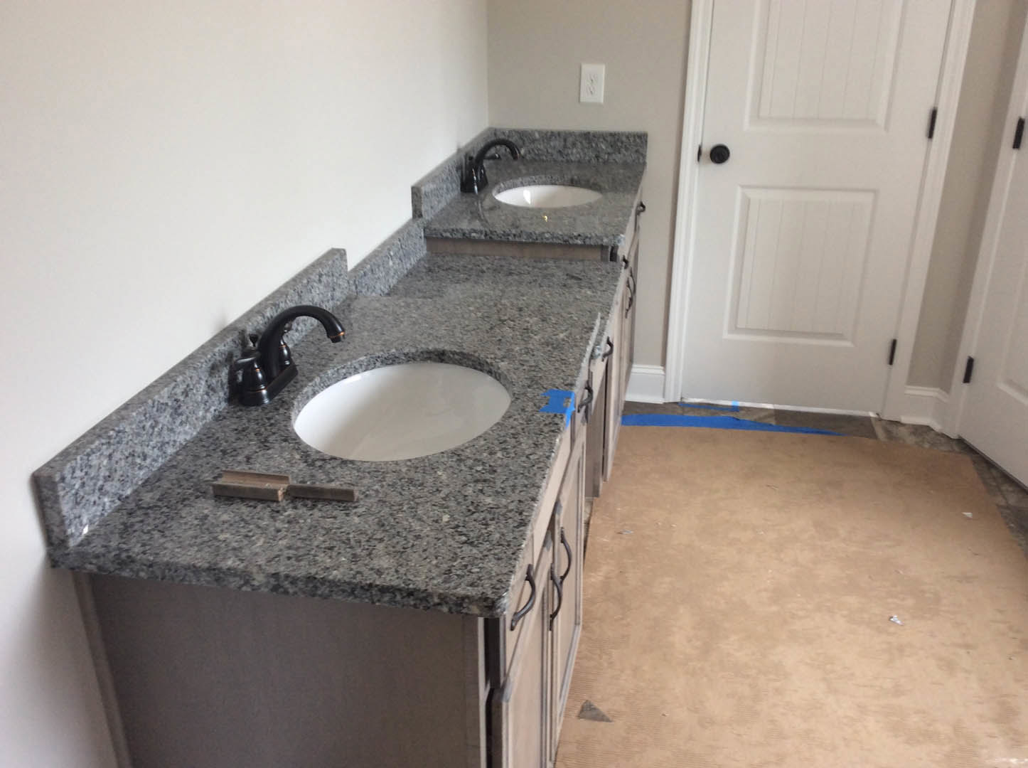 Granite bathroom countertop with black speckled surface, white oval sink, black faucet, white door with black knob, brown carpet visible in adjacent room