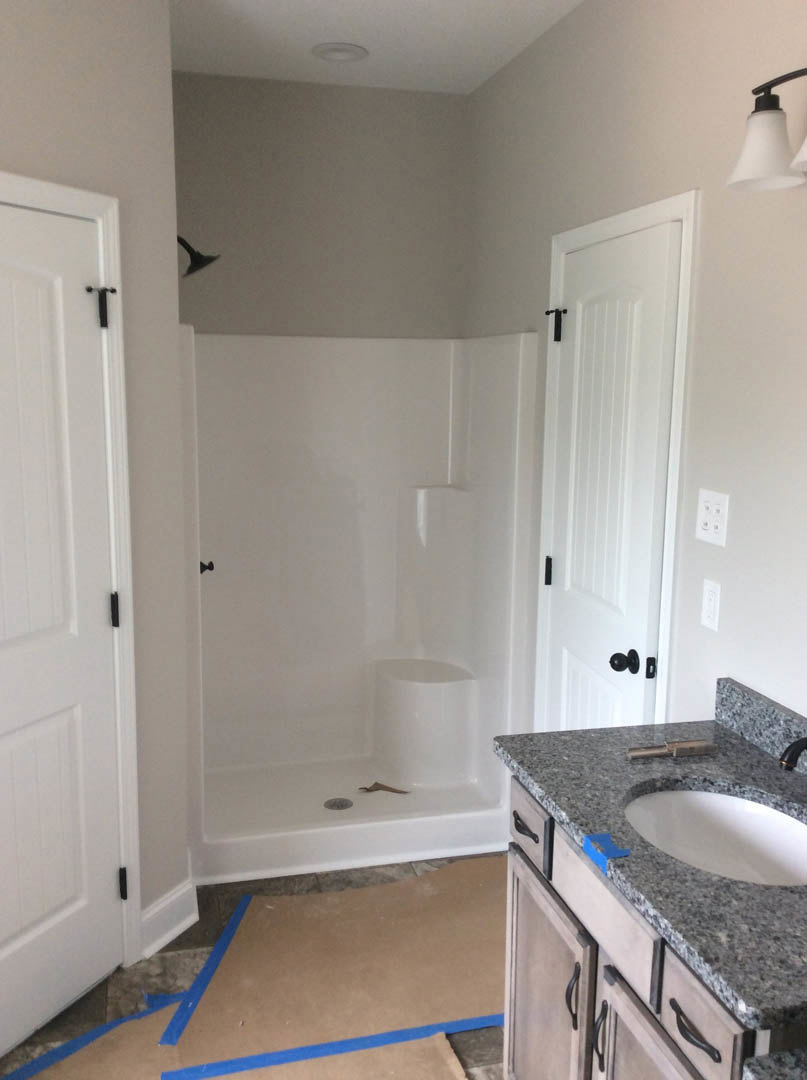 Marble countertop with white oval sink, chrome faucet, blue painter’s tape, soap dispenser, tiled shower, and light-colored cabinetry in a modern bathroom.