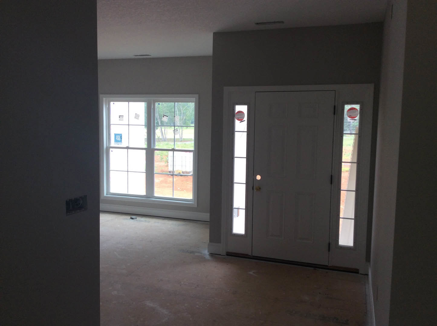 White paneled door with glass inserts, adjacent to large windows with visible stickers, light-colored flooring, and white walls in a residential interior.