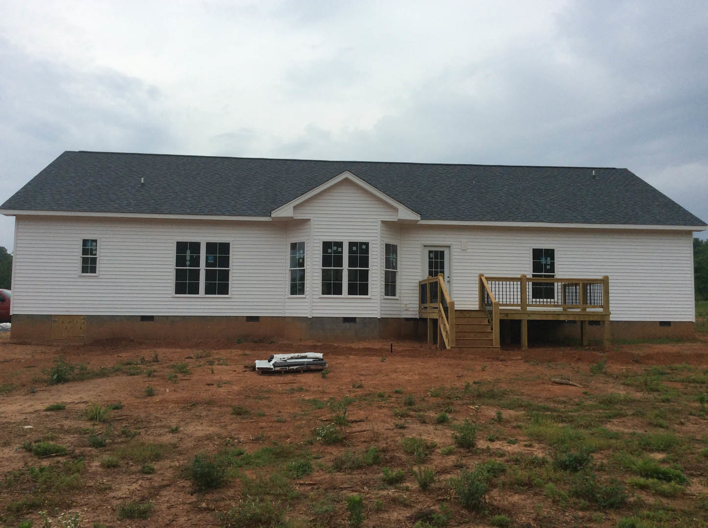 Two-story house with light-colored siding, large windows, wooden deck with metal railing, grassy yard, and covered porch.
