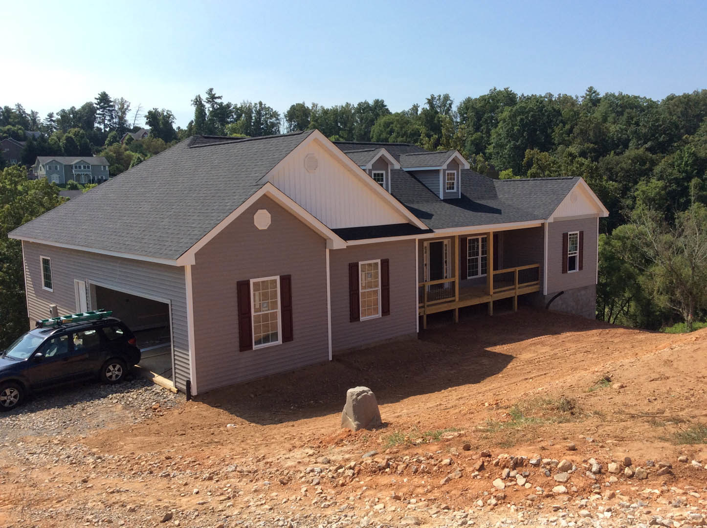 White siding house with attached garage, wooden deck and covered porch, parked SUV with roof ladder on concrete driveway, trimmed lawn, mature trees, blue sky.