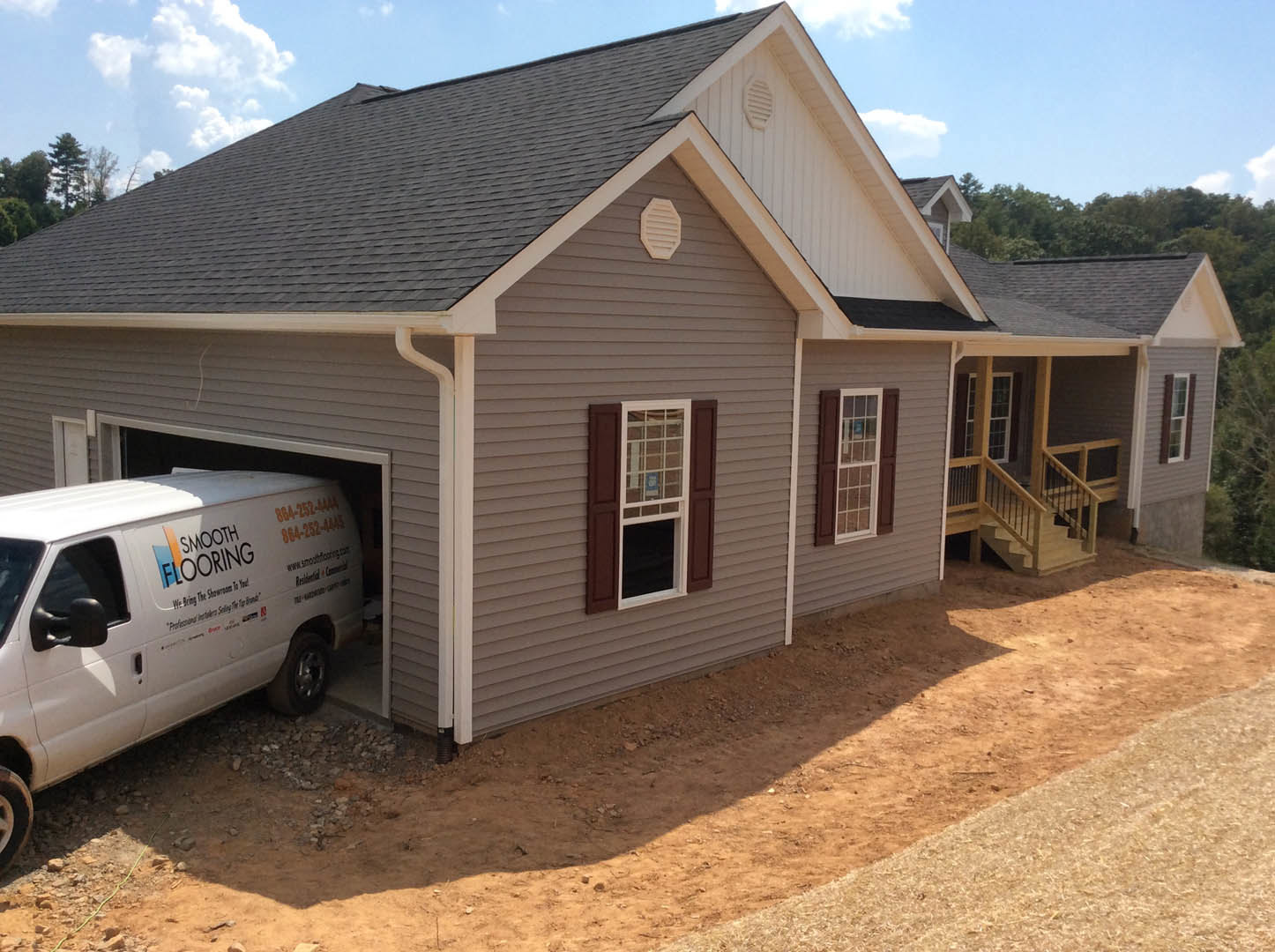 Brown-sided house with open garage revealing a white van, brown shuttered window, white vent, and dirt path alongside exterior.