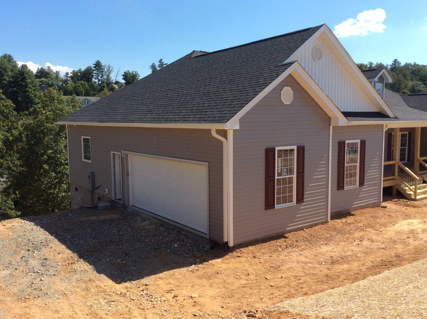 Two-story house with gray roof, white garage door, white-framed windows, white wall vent, and green-leafed tree under a blue sky with clouds