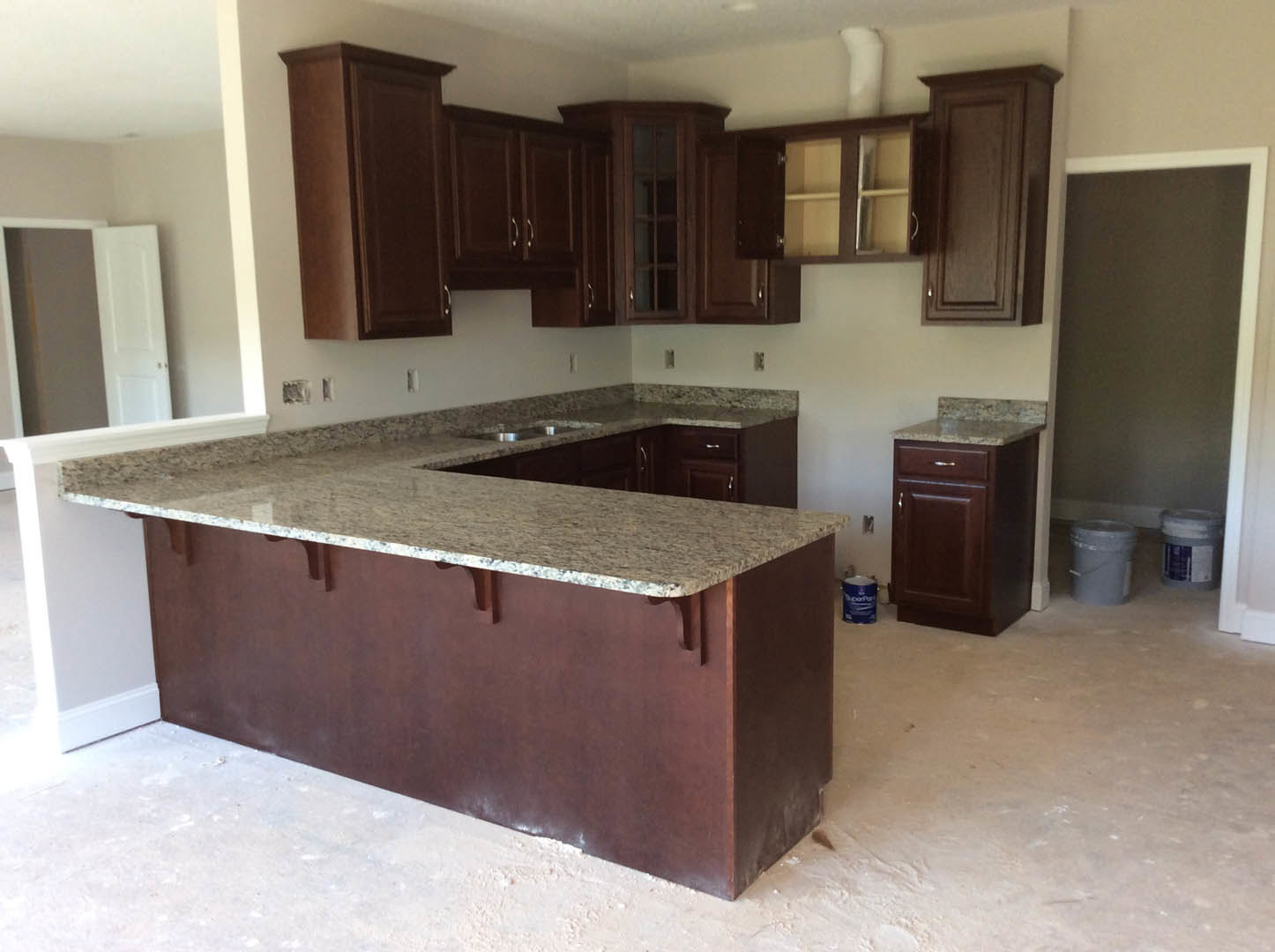 Granite countertop kitchen with white cabinetry, stainless steel sink, tile backsplash, and wood flooring