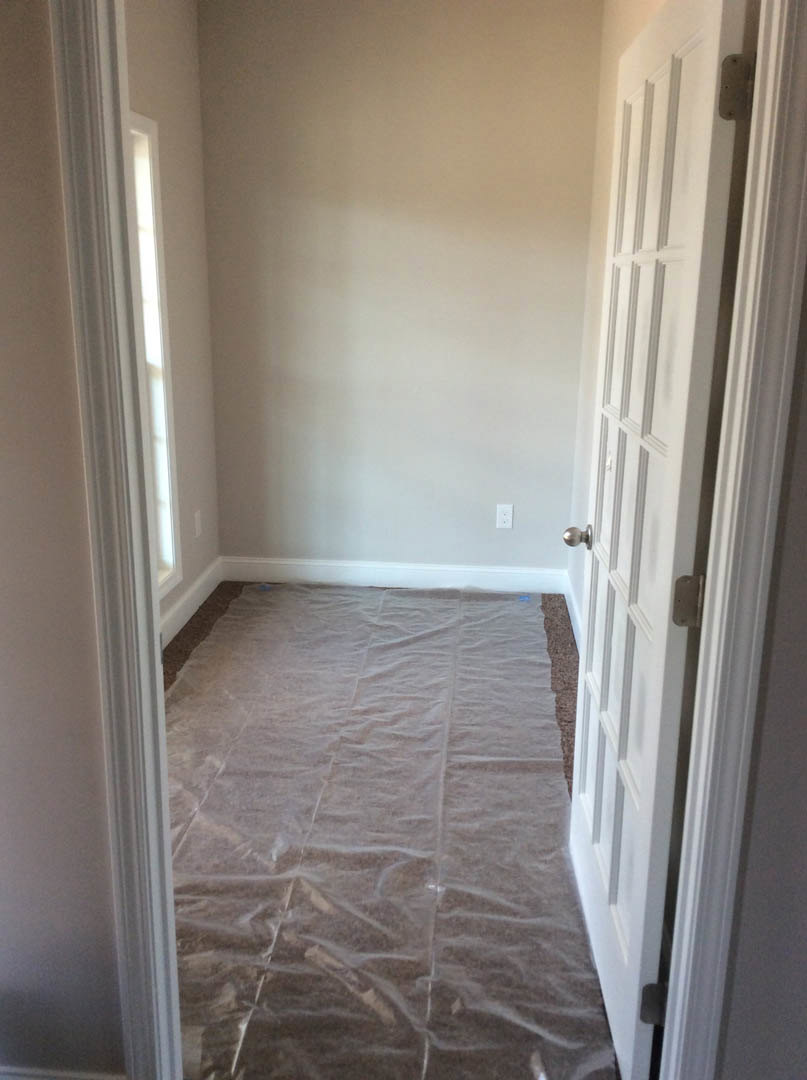 Open doorway leading to a room with white walls and tile flooring, plastic sheet spread across the floor, hallway visible in the background
