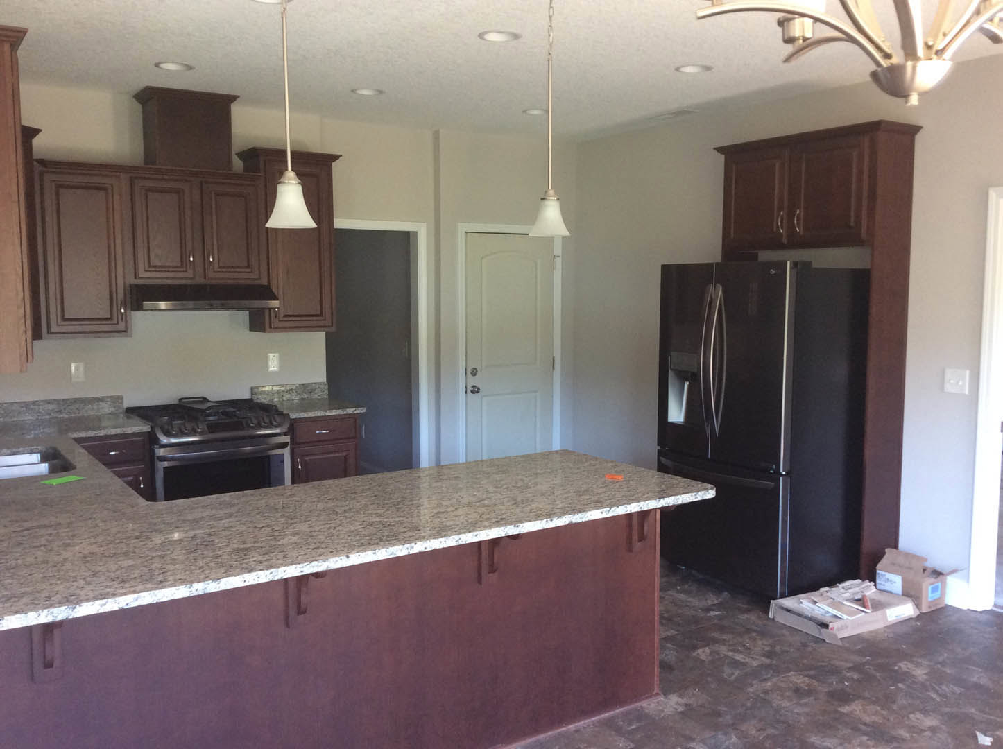 Marble countertop with integrated sink, black refrigerator, white cabinetry, stainless steel stove, and red accent on kitchen island