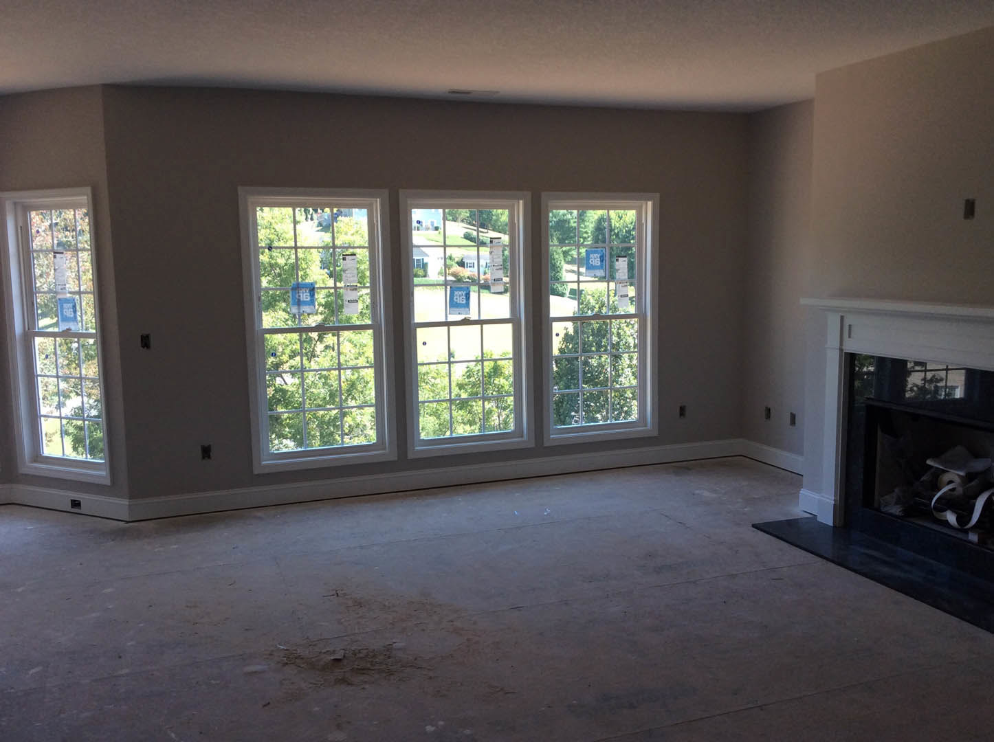 Living room with white-trimmed windows, stone fireplace, hardwood floor, and neutral walls