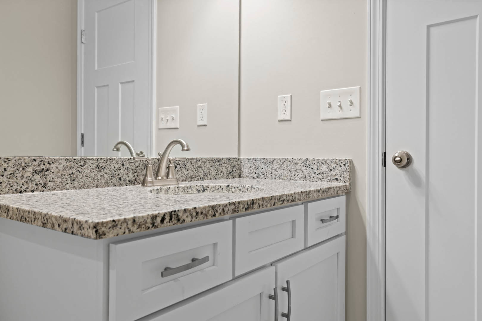 Marble countertop with undermount sink, white shaker cabinets, chrome faucet, white tile backsplash, white door with silver knob, triple light switch, white electrical outlet with