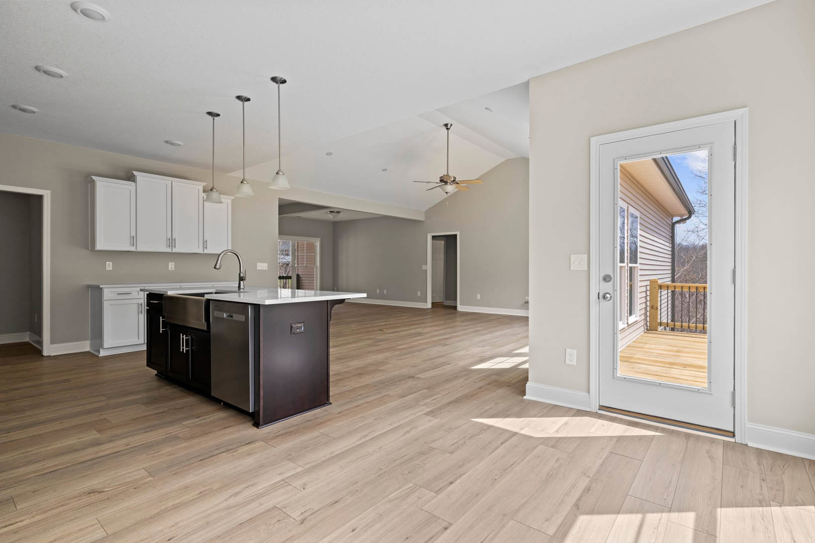 Open-concept kitchen and dining area with wood flooring, white cabinetry, stainless steel sink, white walls, and a door leading to another room