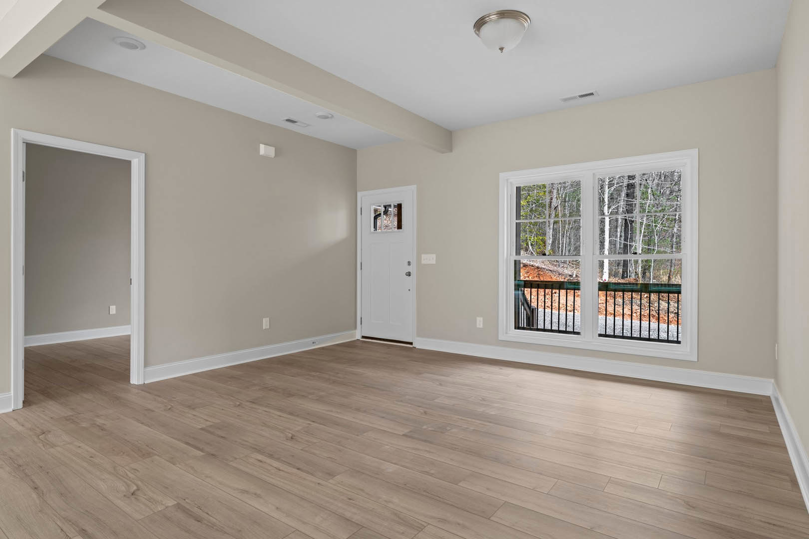 Wood flooring in a room with grey walls, white door with glass panel, and large windows overlooking a forest.