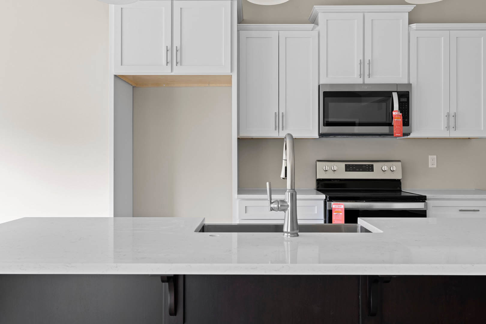 White shaker cabinets, stainless steel sink with chrome faucet, black microwave above matching stove, light quartz countertops, neutral tile backsplash