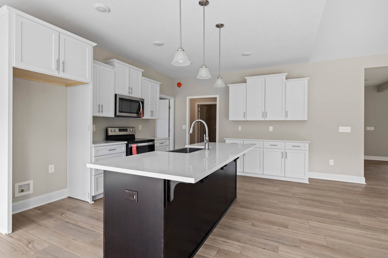 White cabinetry kitchen featuring a black island with built-in sink and faucet, pendant lights overhead, stainless steel microwave, and light-colored flooring.
