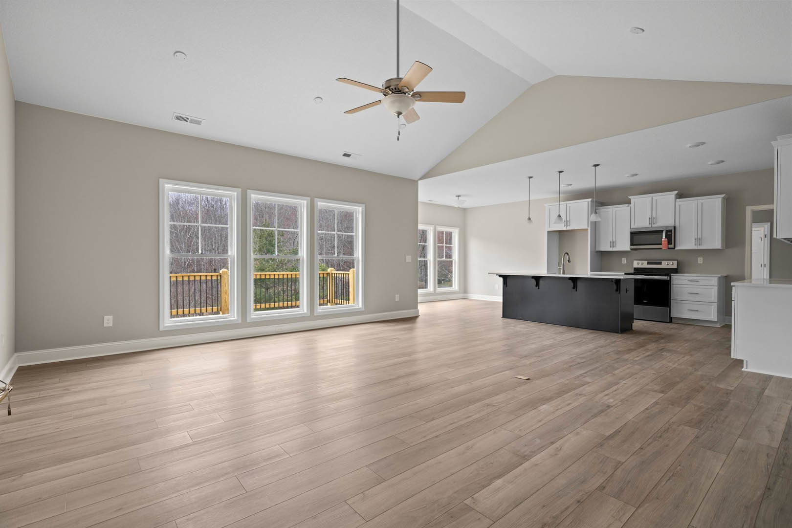 Spacious open floor plan featuring hardwood flooring, kitchen with black cabinetry and white countertops, stainless steel stove and oven, ceiling fan with light fixture, row of