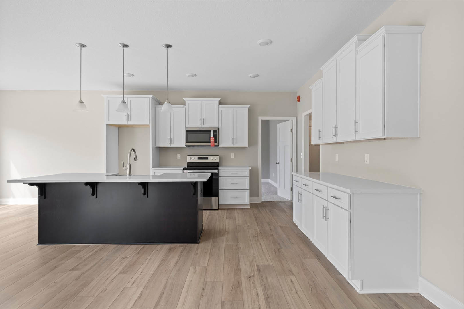 White kitchen cabinets with silver handles, black island featuring a white countertop, stainless steel stove, and a person holding a red object near the sink.