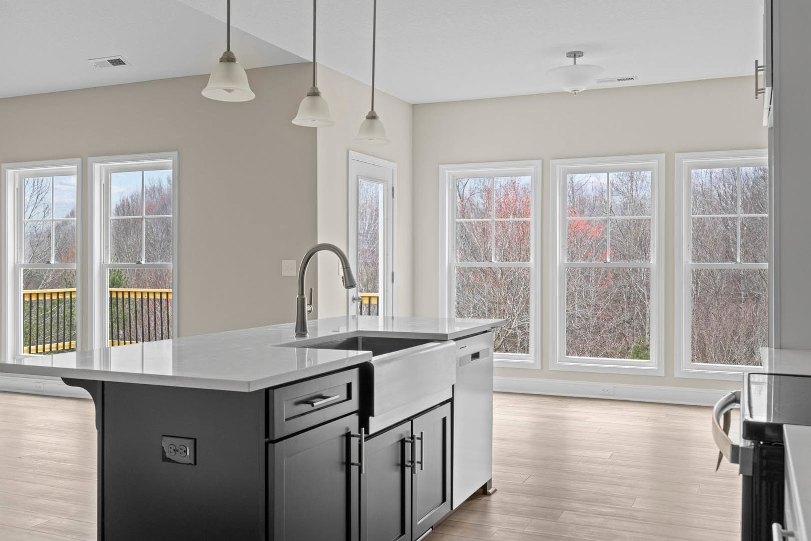 Spacious kitchen featuring a large central island with built-in sink and faucet, white cabinetry, stone countertops, and windows overlooking green trees