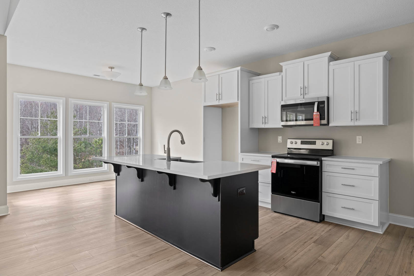 Kitchen featuring a black island with white cabinets, white countertops, stainless steel stove and oven, silver drawer handles, windows overlooking trees, and a fire extinguisher