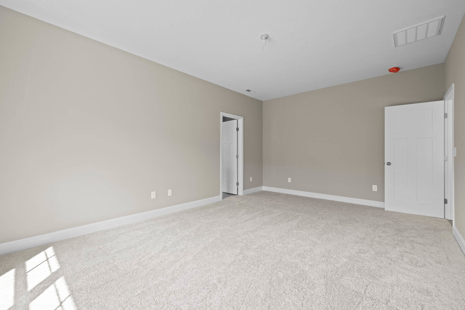 White carpeted room with multiple windows, open white door featuring a silver knob and cross detail, white ladder leaning against a plaster wall.