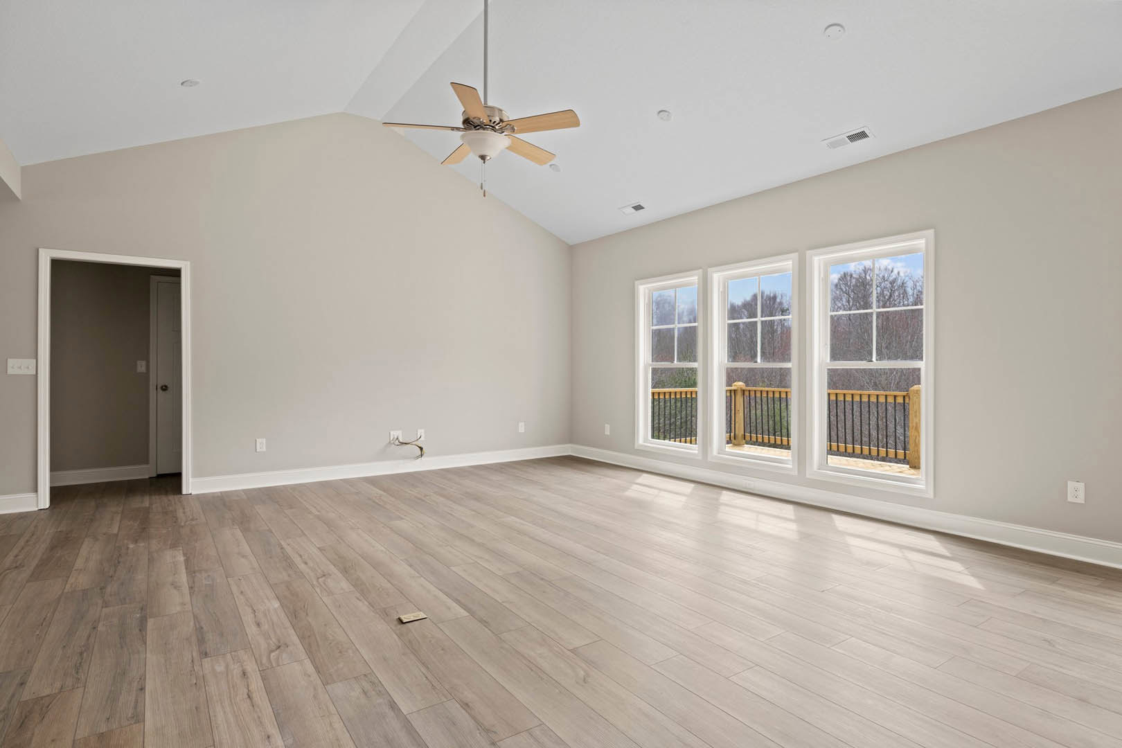 Hardwood flooring, white walls, ceiling fan with light fixture, large windows, white-framed door, and metal railing in a bright interior room