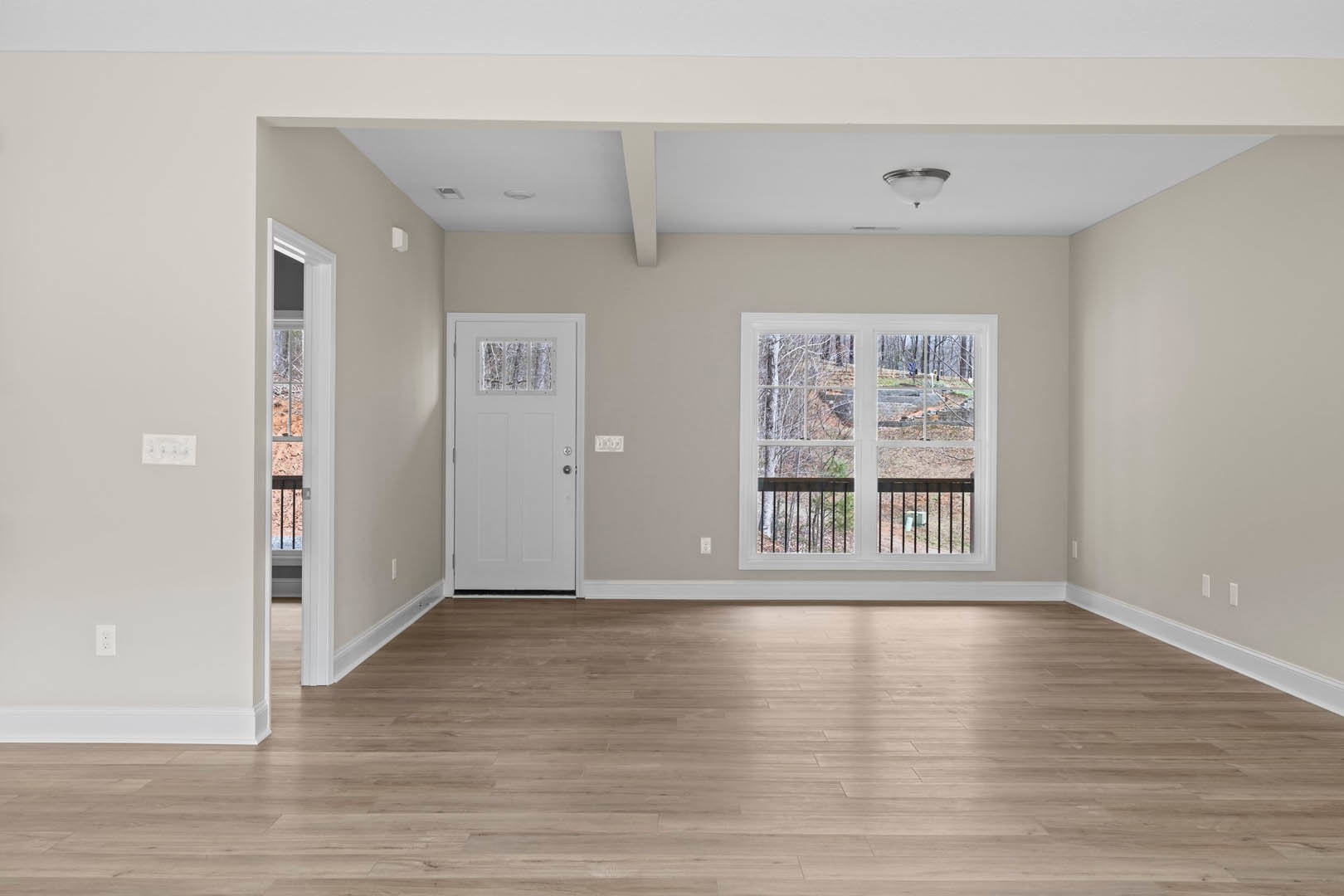 Wood flooring and white plaster walls in a room featuring a white door with a glass panel and large windows overlooking a forest.