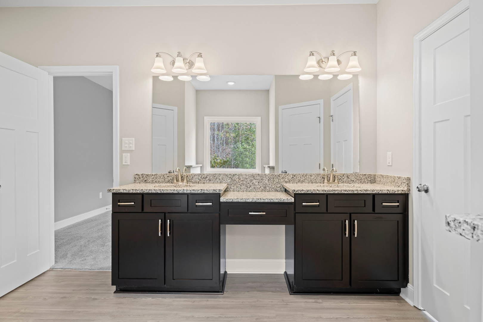 Double sink vanity with black cabinets and drawers, white countertop, tile flooring, white walls, modern light fixture, window overlooking trees, white door with silver handle