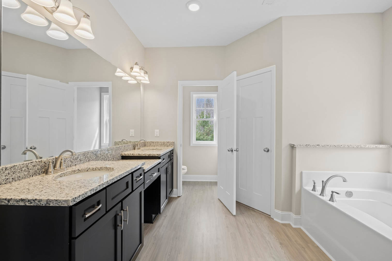 Bathroom featuring marble countertops, freestanding bathtub with chrome faucets, wood flooring, large window overlooking trees, white door with silver hardware, and modern sink