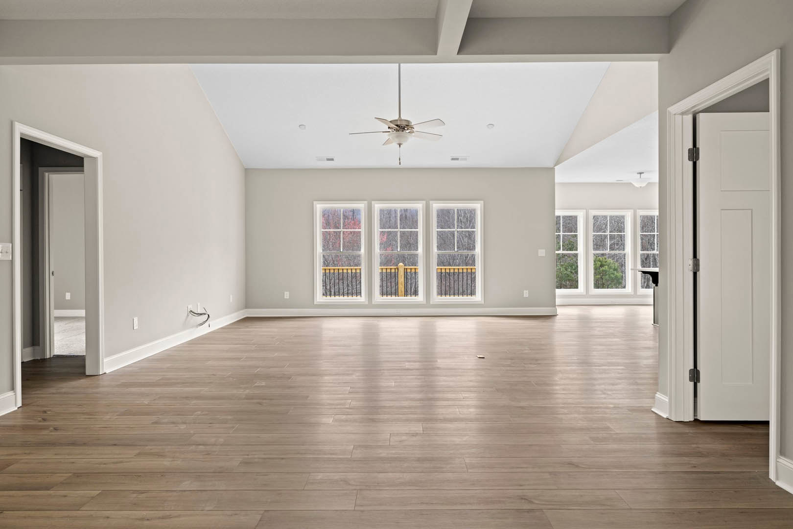 Spacious room featuring wood flooring, row of windows with white trim and railing, ceiling fan with light fixture, and white door with metal lock