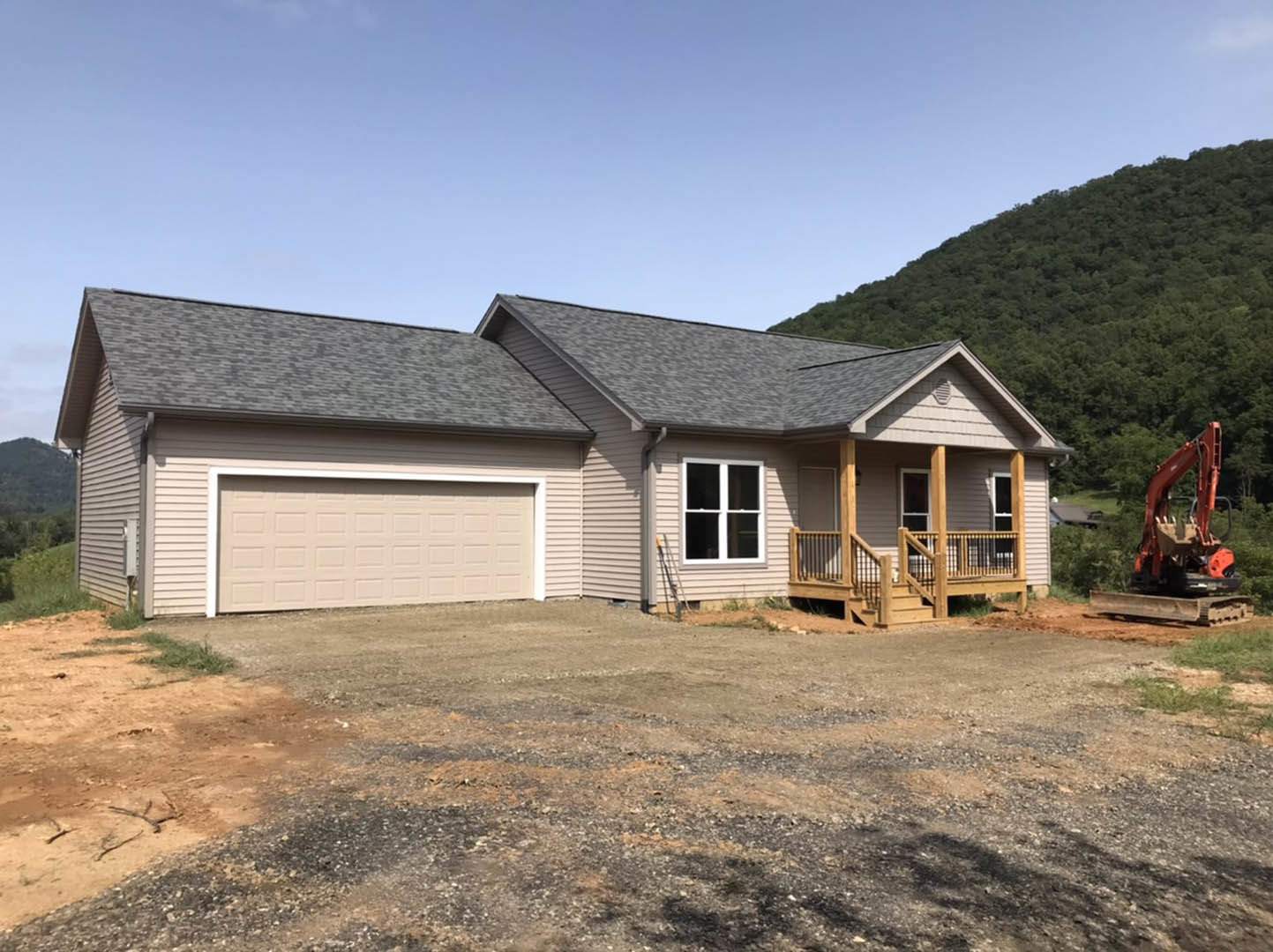 White garage door and driveway leading to a modern house with white-framed windows, light siding, and a gravel area in front; construction vehicle parked near the entrance.