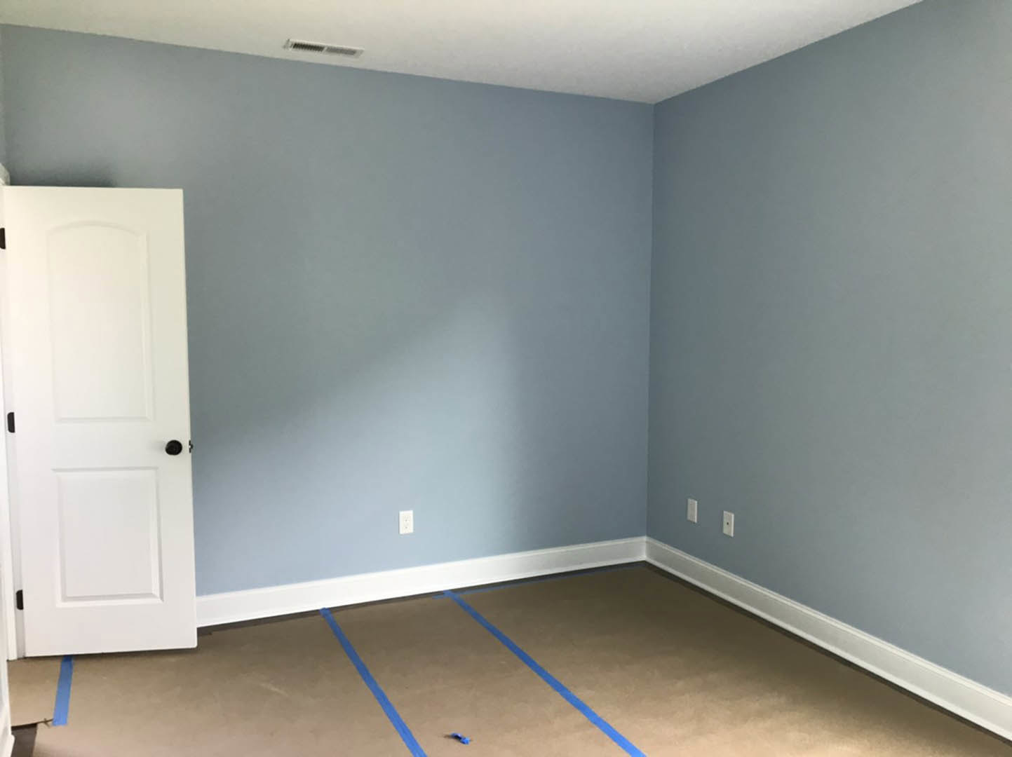 Blue-painted walls, white door with black knob, laminate flooring with blue tape, white electrical switches, white rectangular object with black border.