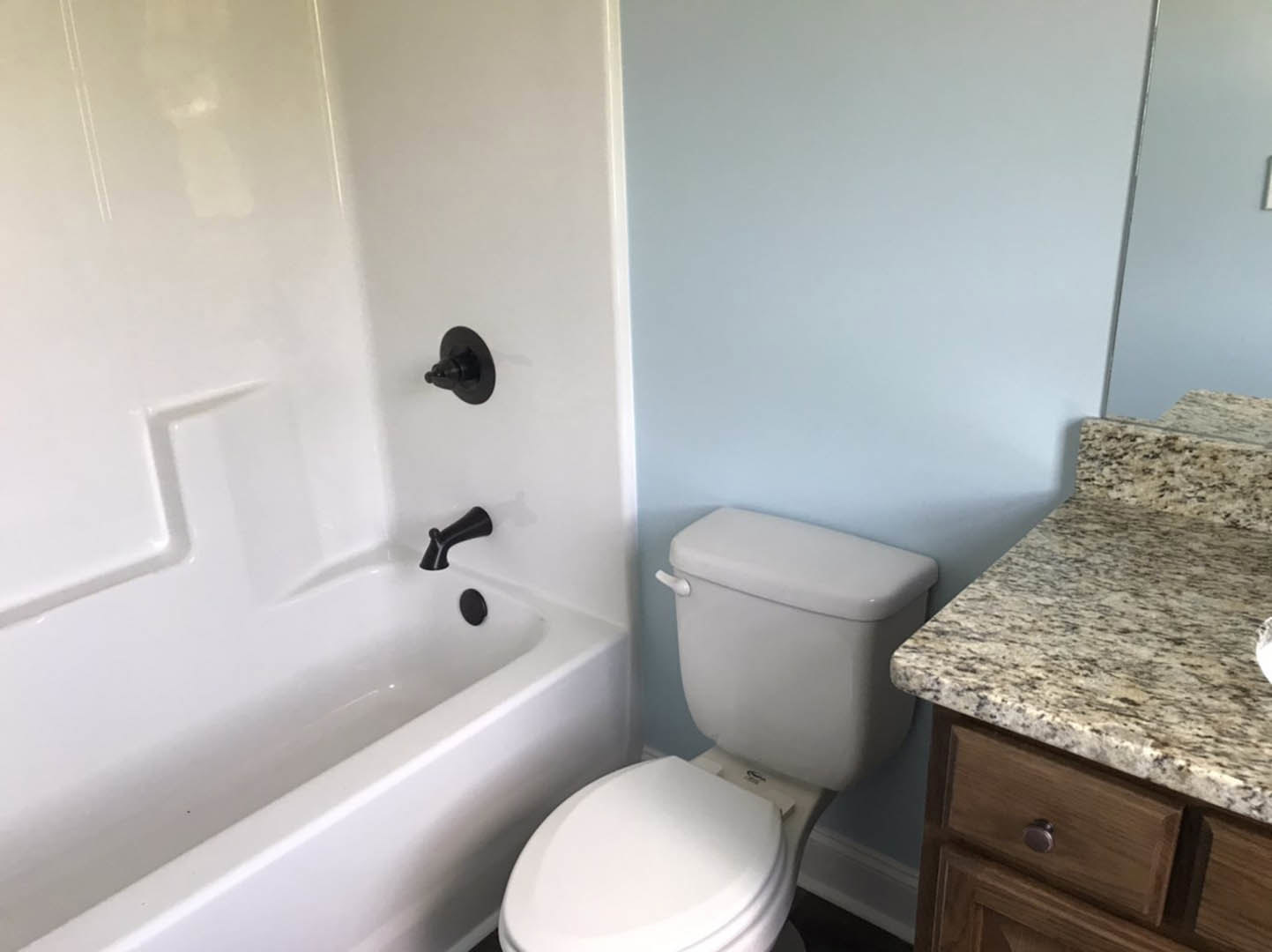 White bathroom with modern black faucet, rectangular sink on white countertop, blue accent wall, white toilet, and white bathtub with black fixtures.