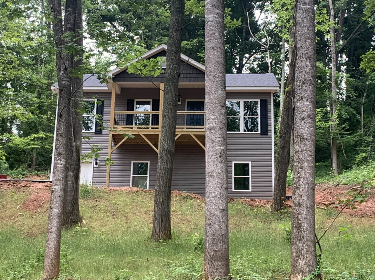 Two-story cottage-style home with white-framed windows, white porch railing, and mature trees surrounding the grassy yard