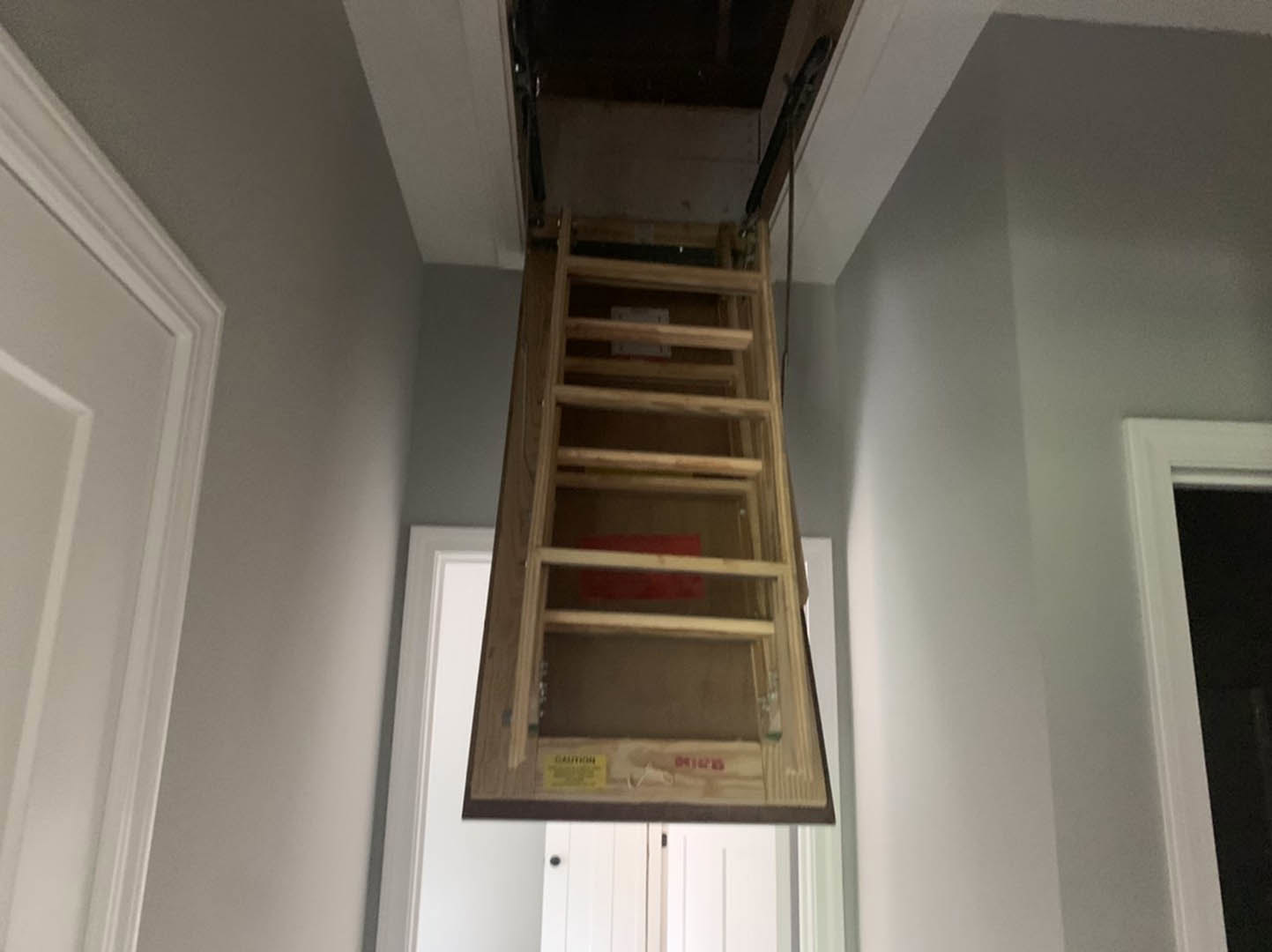 Wood ladder leaning against white plaster wall beside built-in wooden shelf with glass doors in a bright room with crown molding and ceiling fixture