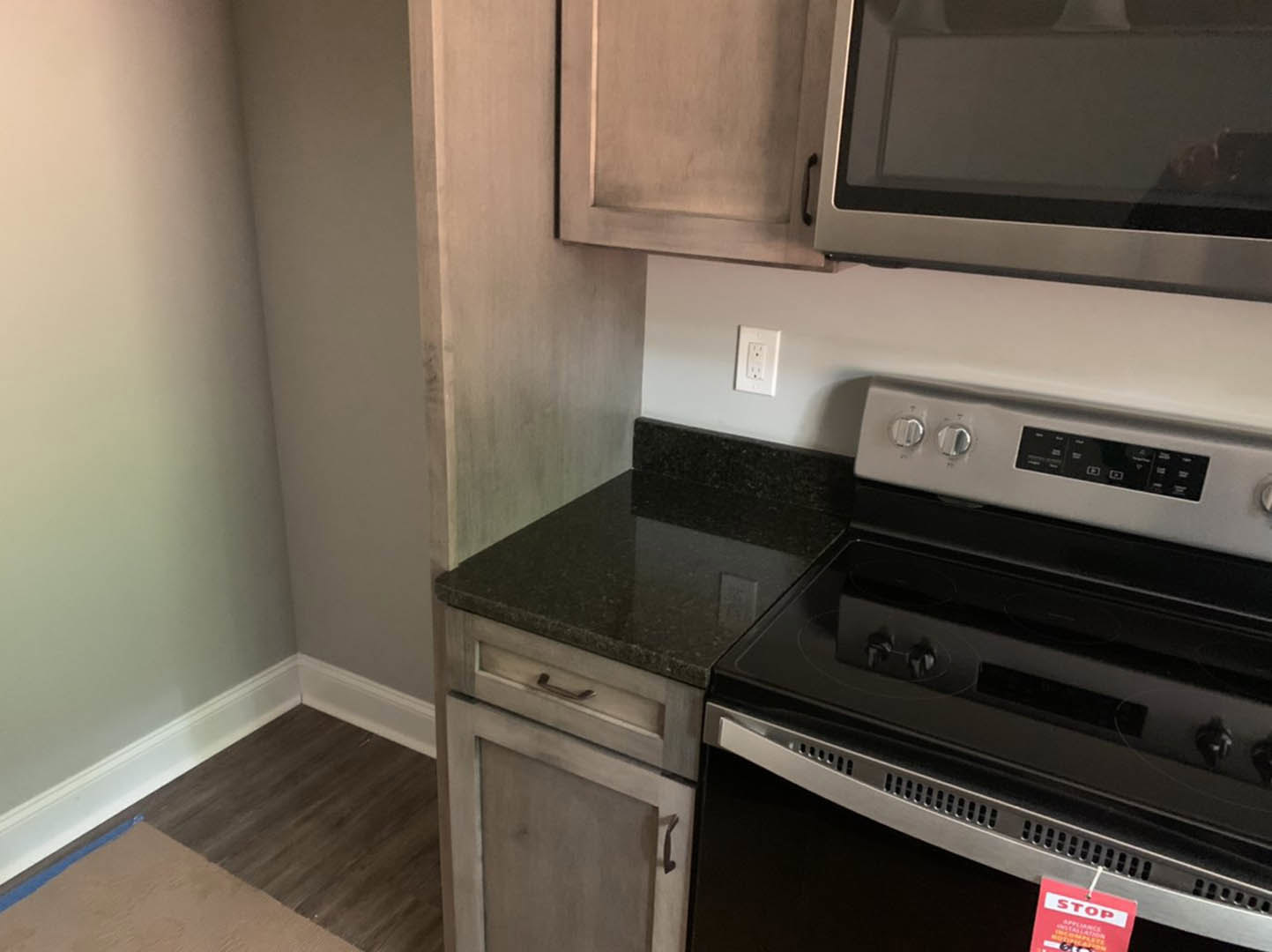 White shaker cabinets and stainless steel microwave oven above a matching stove, light quartz countertops, subway tile backsplash, electrical outlet on wall