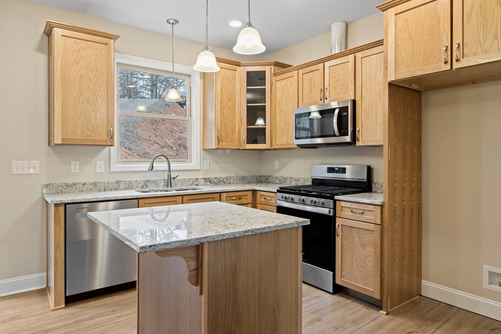 Marble kitchen island with built-in sink, white cabinetry, stainless steel microwave, wooden door, and window overlooking dirt hill