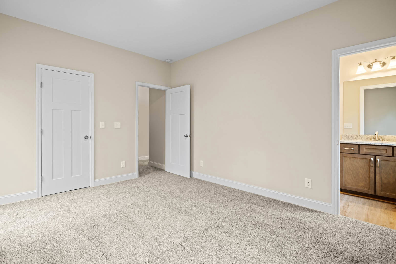 Carpeted room with two white doors featuring silver knobs, white walls, and partial view of a kitchen cabinet