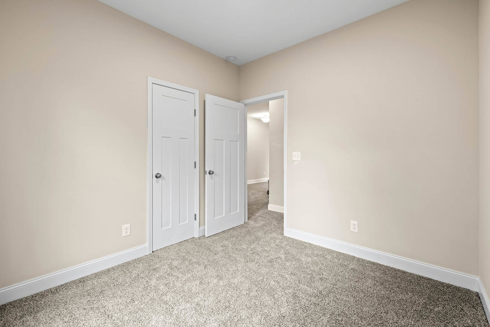 White carpeted room featuring multiple white paneled doors with silver knobs, white walls, side wall sconce, and white ceiling with a fire alarm.