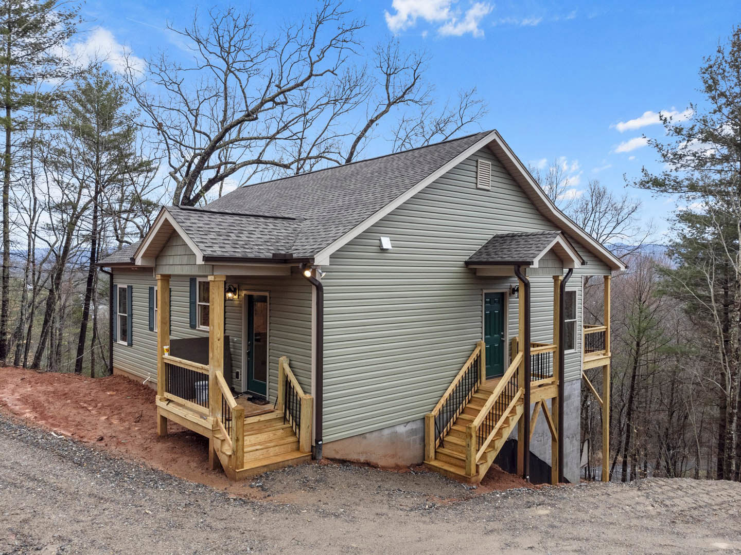 Wooden stairs with railing leading up to a side porch entrance on a log cabin-style home, surrounded by trees and cloudy sky.
