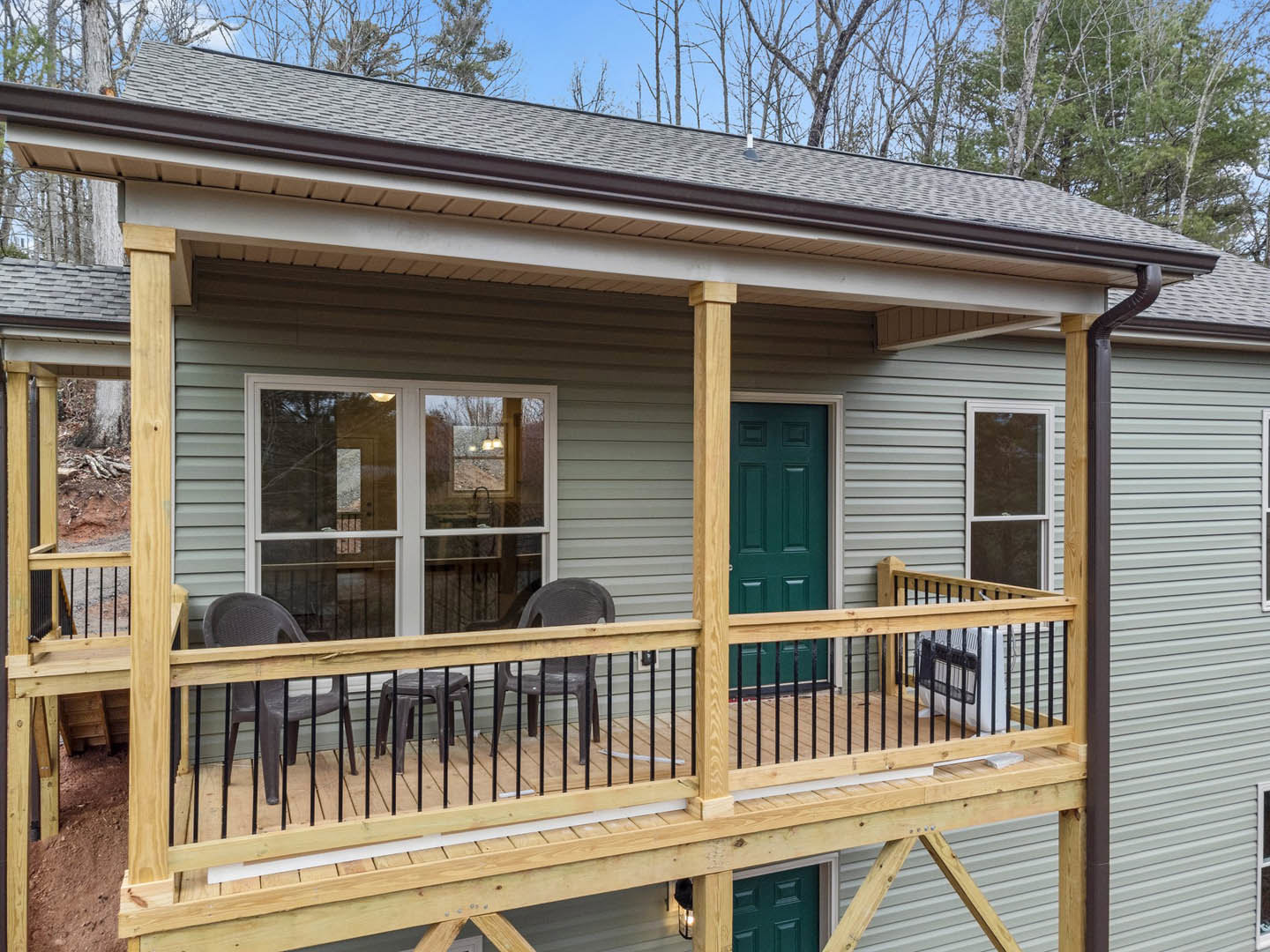 Wood deck with metal railing, two outdoor chairs, green front door, large windows, light siding exterior