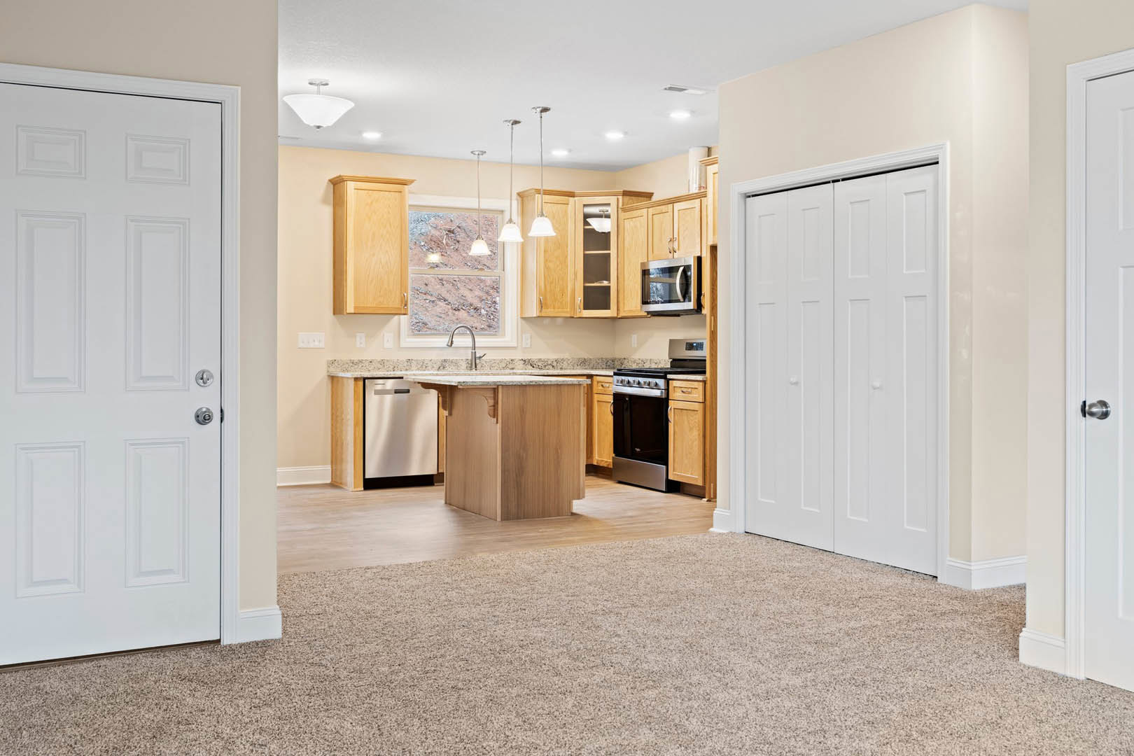Open-concept kitchen and living room featuring carpeted flooring, white cabinetry, built-in microwave, white interior doors, and black lower cabinets.