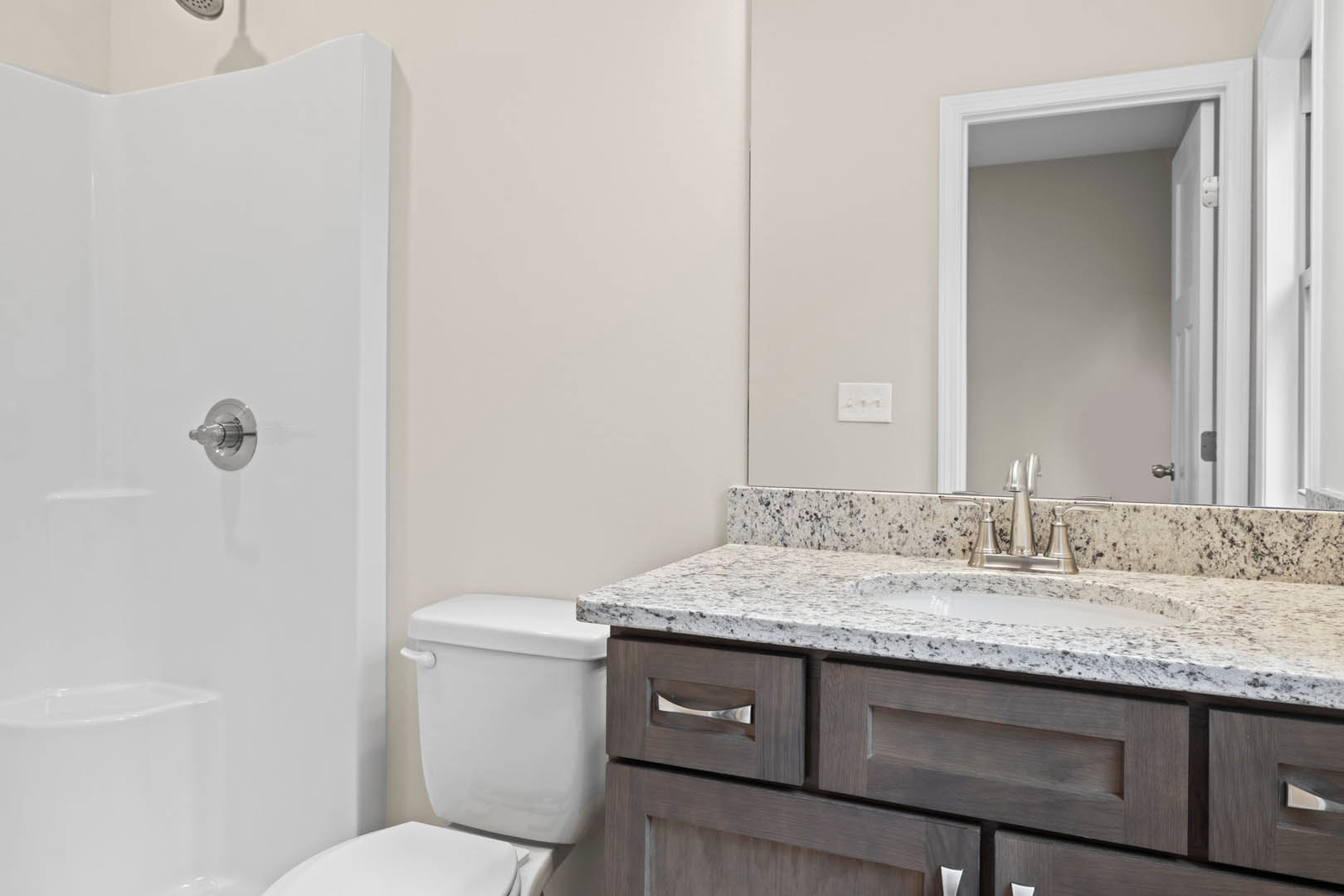 Modern bathroom featuring white ceramic sink and toilet, light gray tile walls, chrome shower knob, three-switch white light plate, white door with matching frame, and built-in