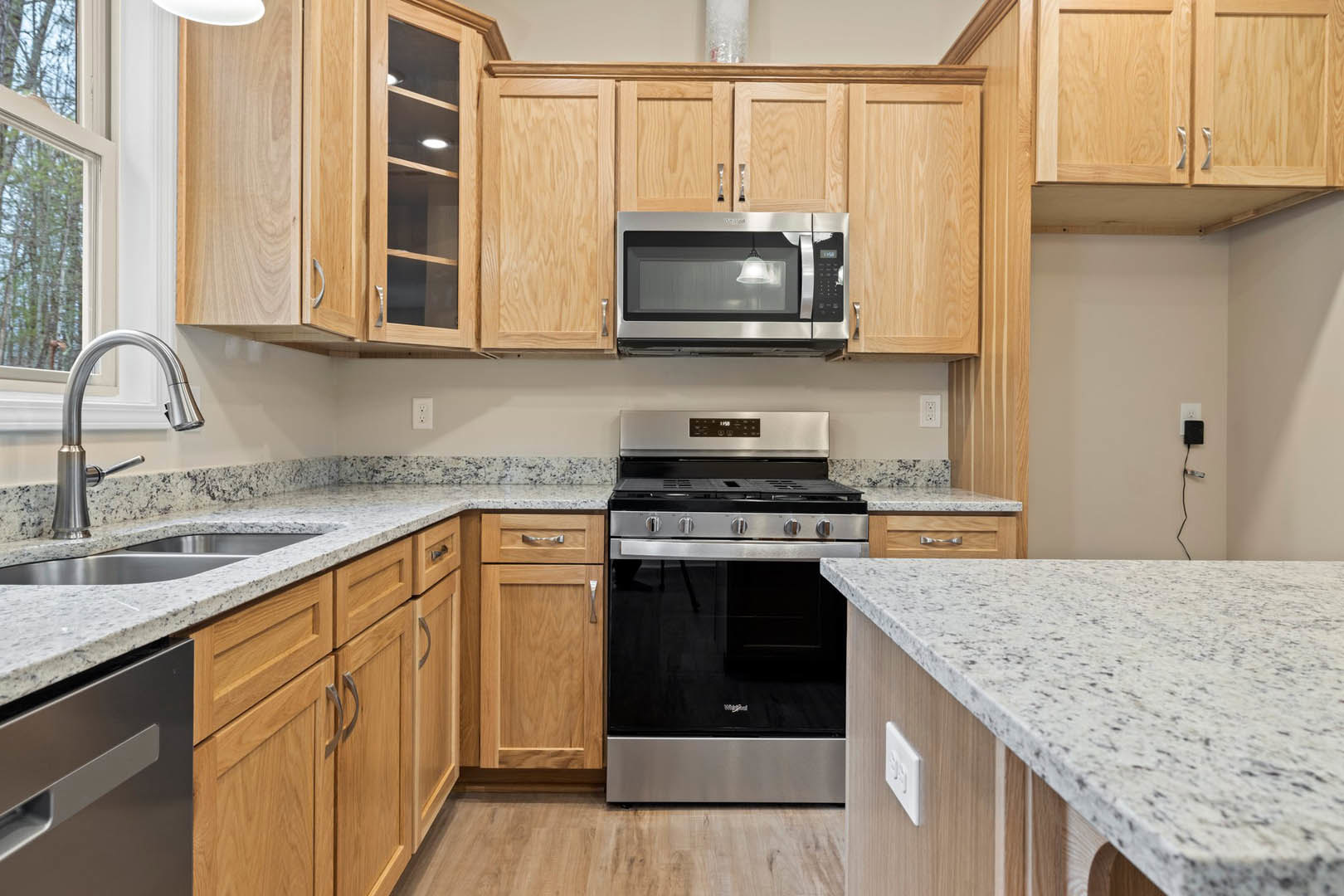 Kitchen with medium-tone wooden cabinets, stainless microwave above a black stove, stone countertop, chrome faucet, and drawer front visible