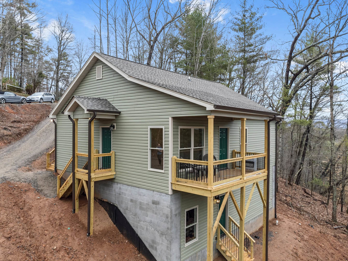 Two-story custom home with light siding, wooden deck, and exterior staircase; large windows, railing, and landscaped yard with trees visible.