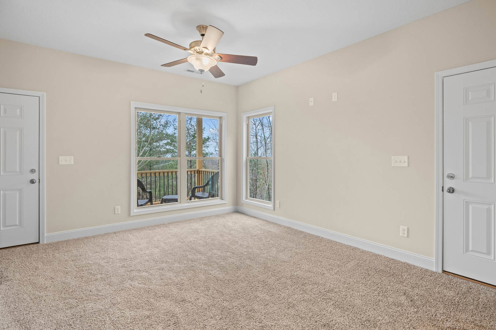Carpeted room featuring a ceiling fan with light fixture, white door, large windows overlooking a deck with chairs, plaster walls, and crown molding.