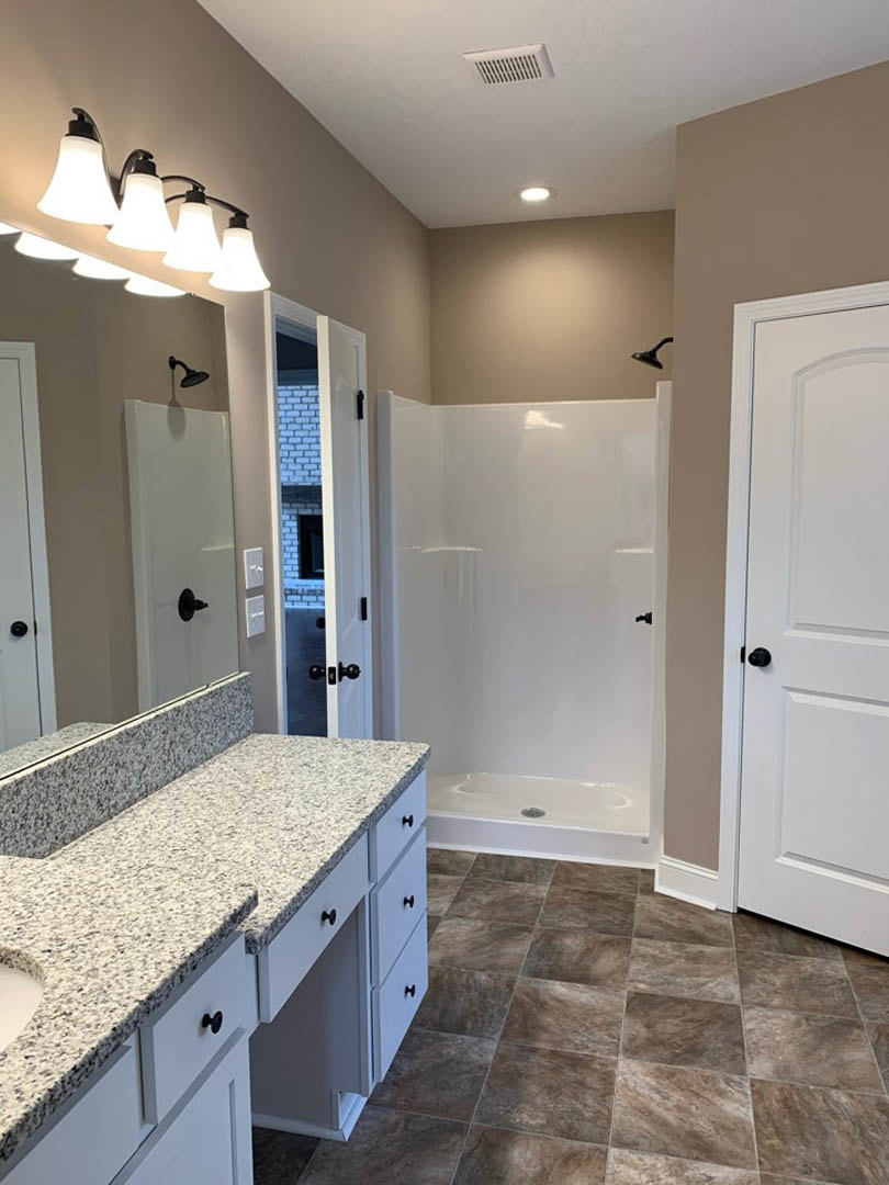 Bathroom featuring a marble countertop with undermount sink, glass-enclosed shower, white door, tile flooring, and wall-mounted row of lights