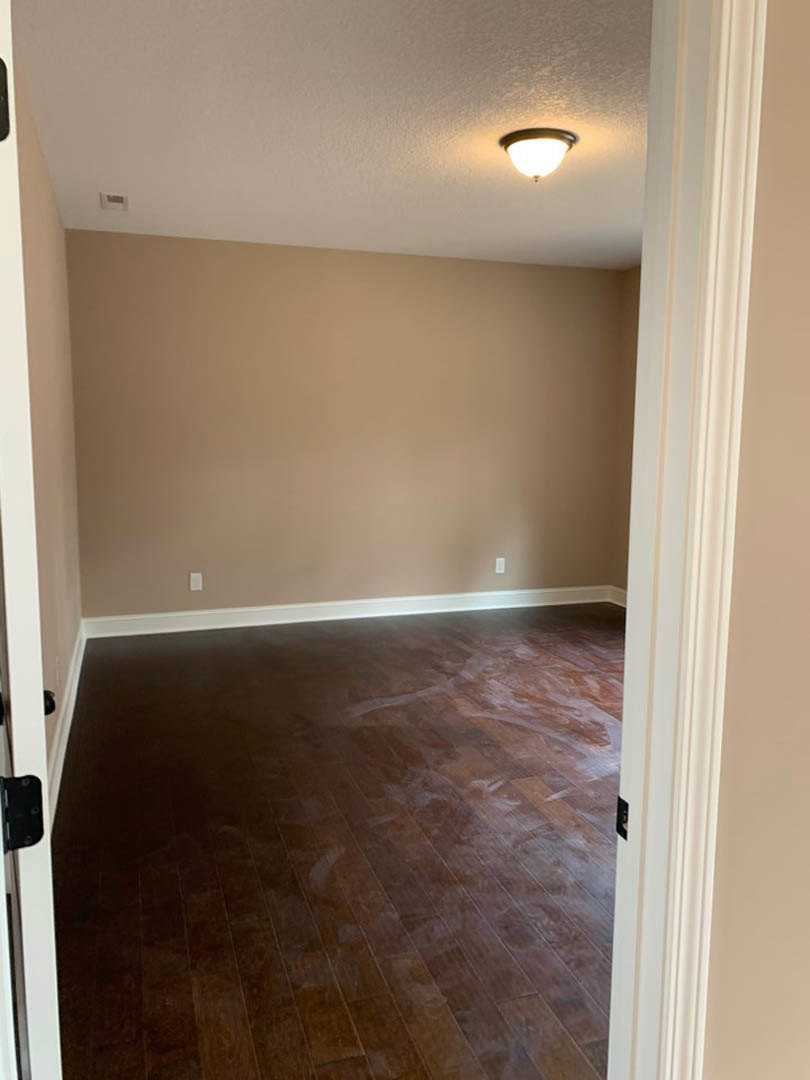 Hardwood floor with white painted walls, beige accent wall, ceiling-mounted light fixture, white column, and black metal-framed object in a custom home interior.