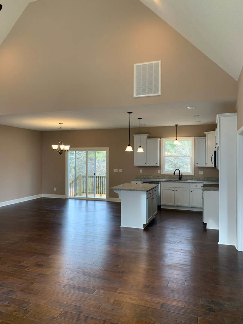 Hardwood floors throughout kitchen and dining area, white kitchen island with marble countertop, stainless steel sink beneath window, pendant light fixture, sliding glass door with