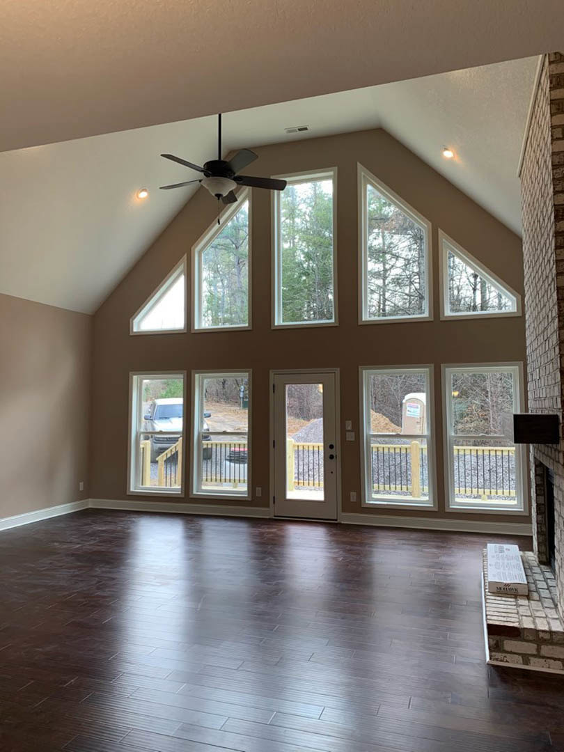 Living room with hardwood floors, stone fireplace, ceiling fan with light fixture, large windows, and glass doors leading outside