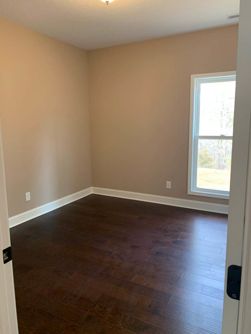 Sunlit room featuring a large white-framed window, dark hardwood flooring, and smooth plaster walls