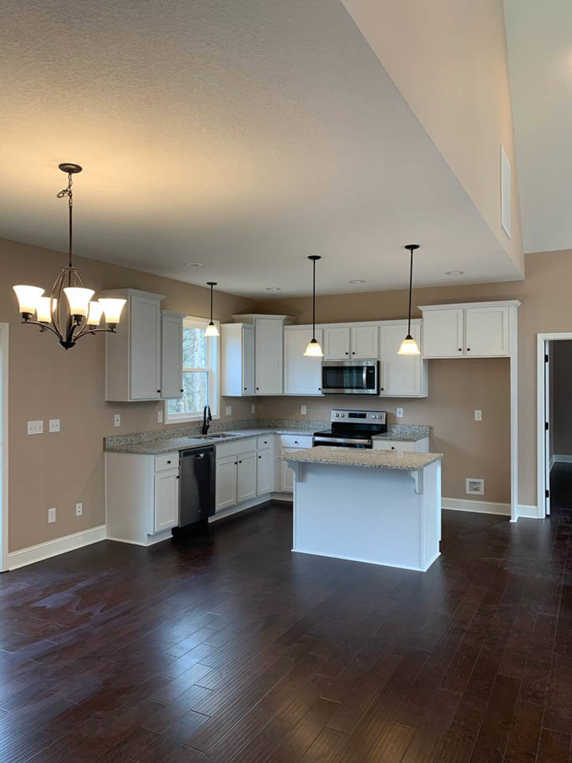 Spacious kitchen featuring a large central island with white granite countertop, dark wood flooring, white cabinetry, stainless steel appliances, and a modern chandelier overhead.