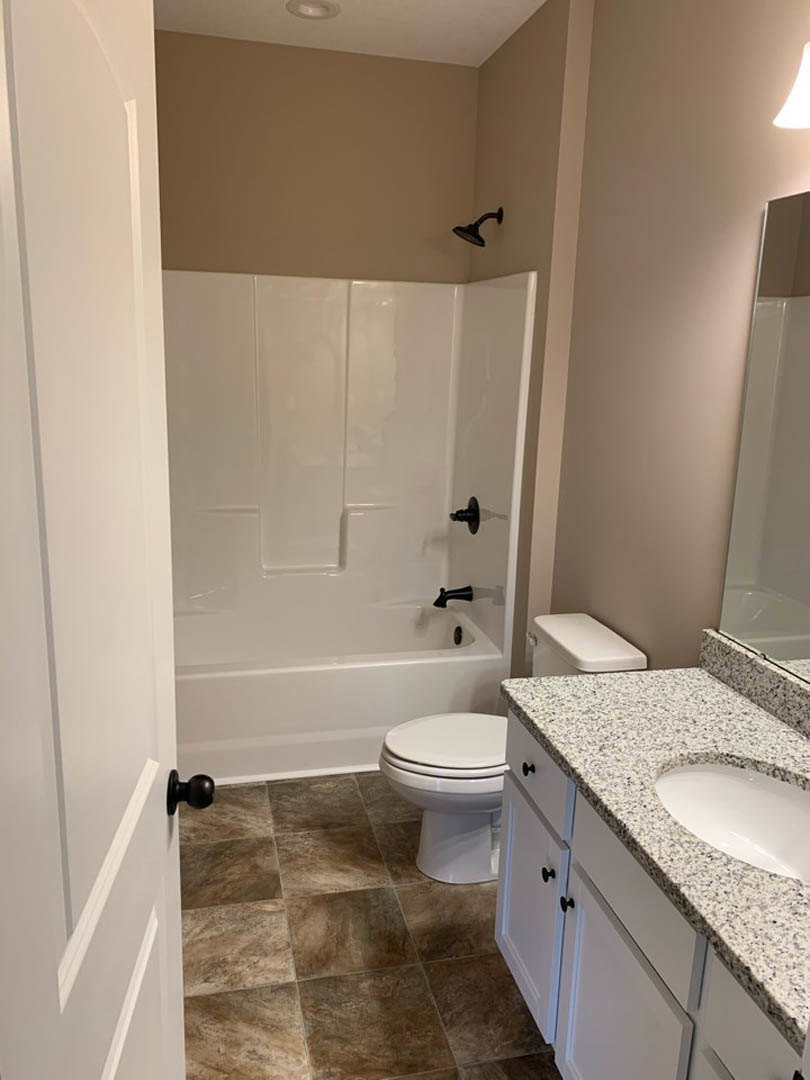 White bathroom featuring a freestanding tub with matte black faucets, white sink with black hardware, wall-mounted shower head, and a black door knob on a white door.